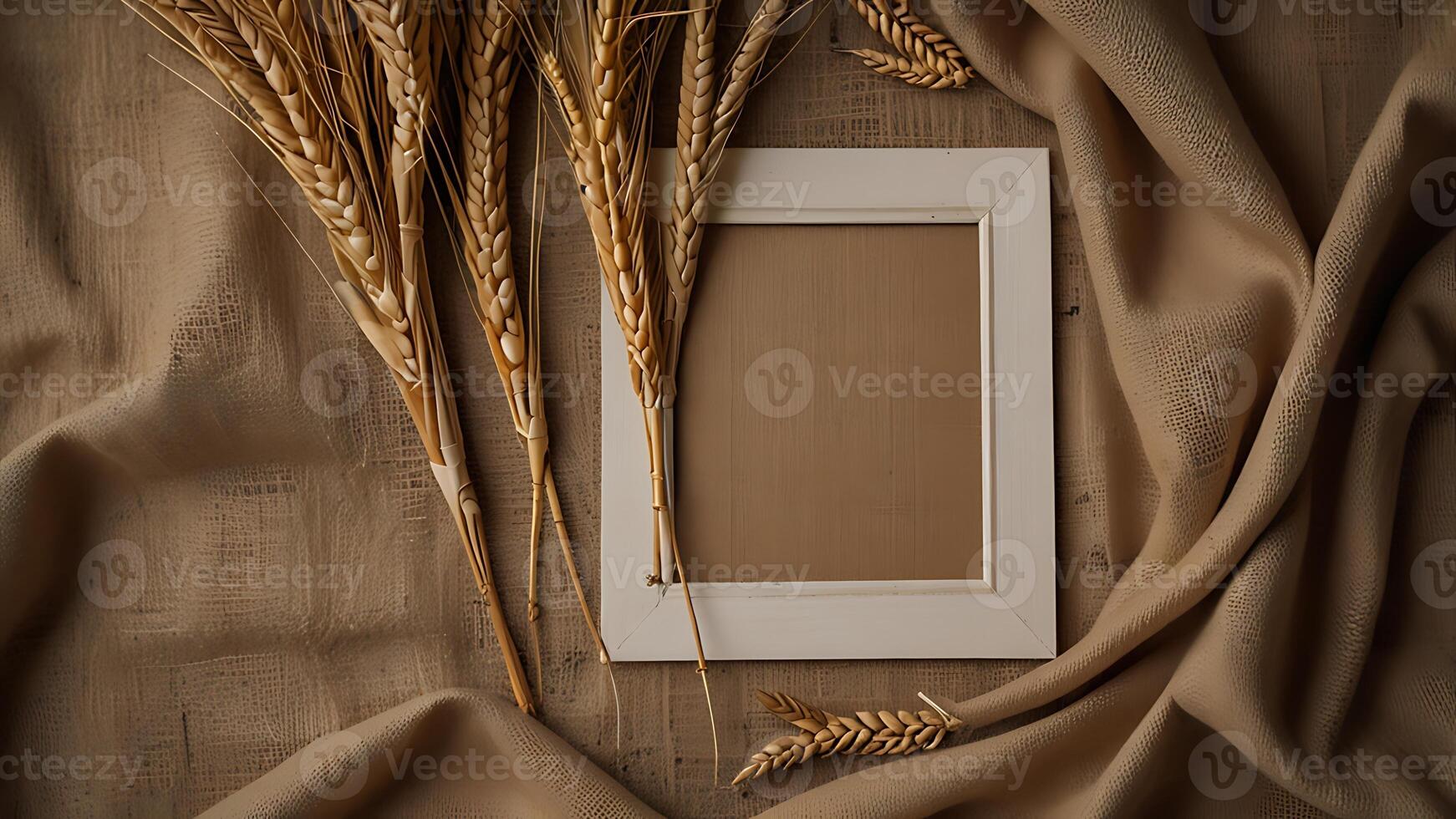 Wheat stalks frame a blank white picture frame against a textured tan fabric for a business project photo