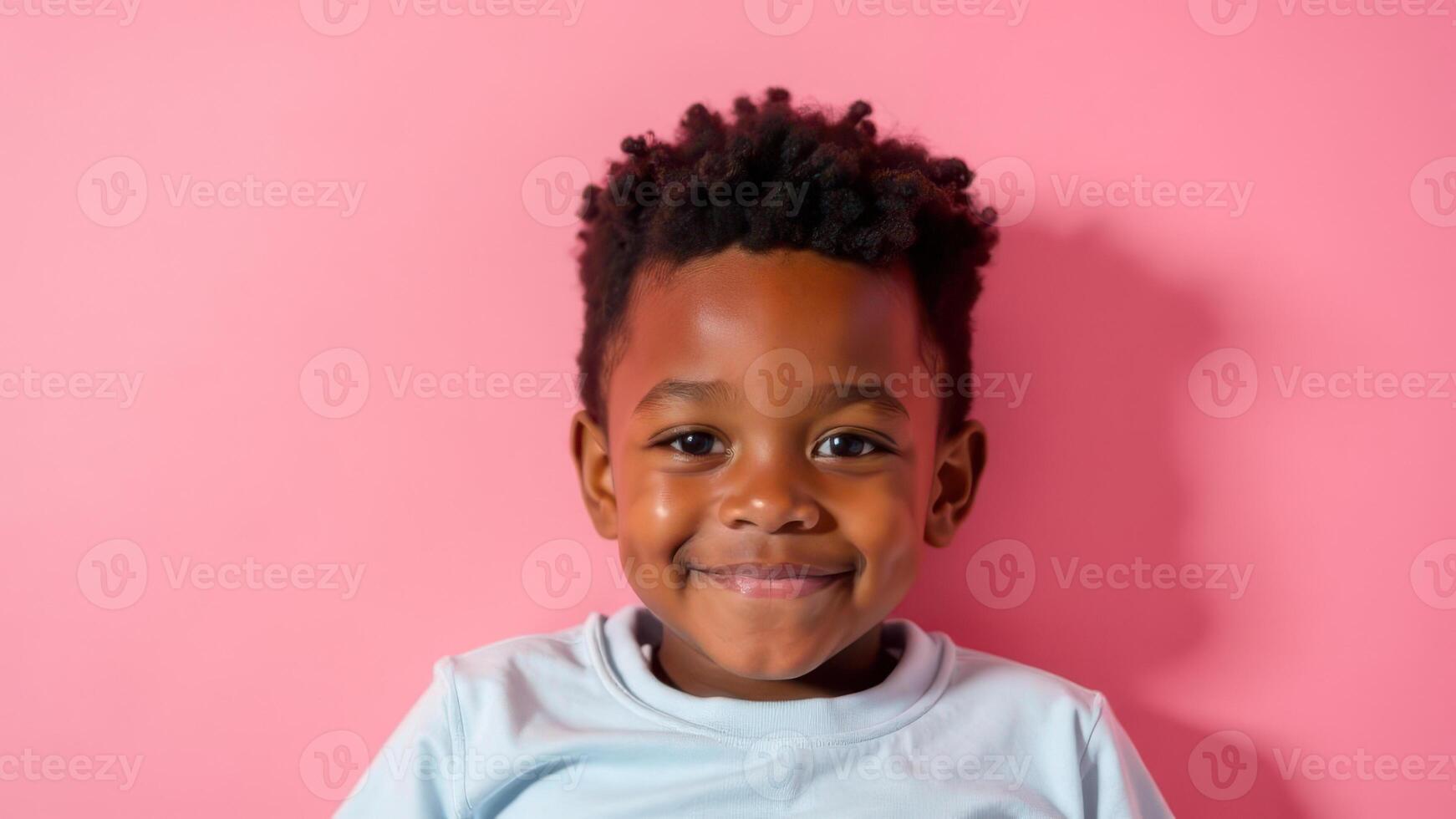A smiling boy in a blue shirt poses confidently against a pink background photo