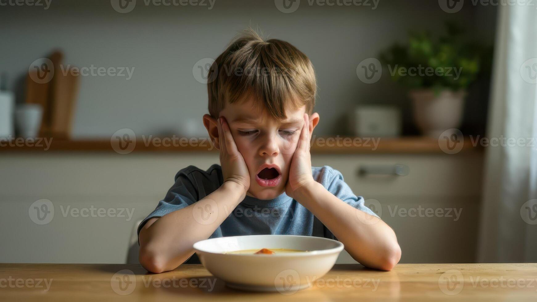 A little boy with a displeased expression stares unhappily at a bowl of soup photo