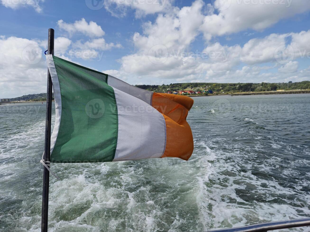 Irish Flag Fluttering Above a Scenic River Backdrop photo