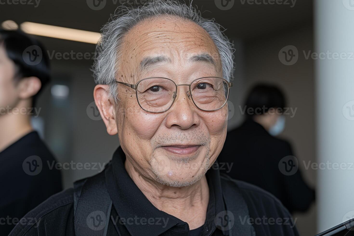 Close-up of a cheerful elderly asian man wearing glasses and a black shirt, captured in a casual indoor environment. photo