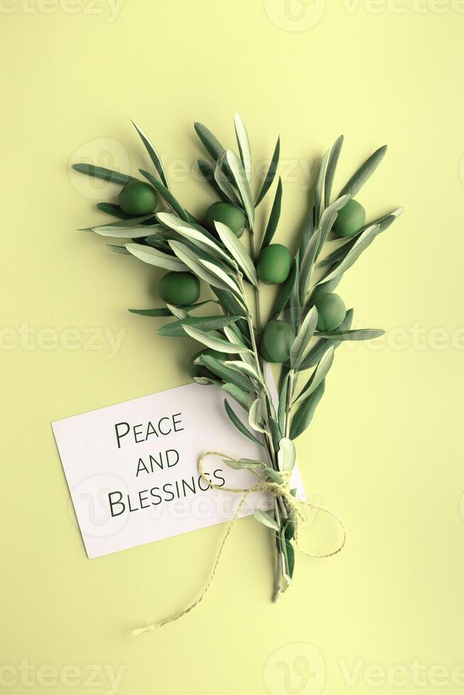 Olive branch with green olives and blank card on light yellow background. Peace and blessings. photo