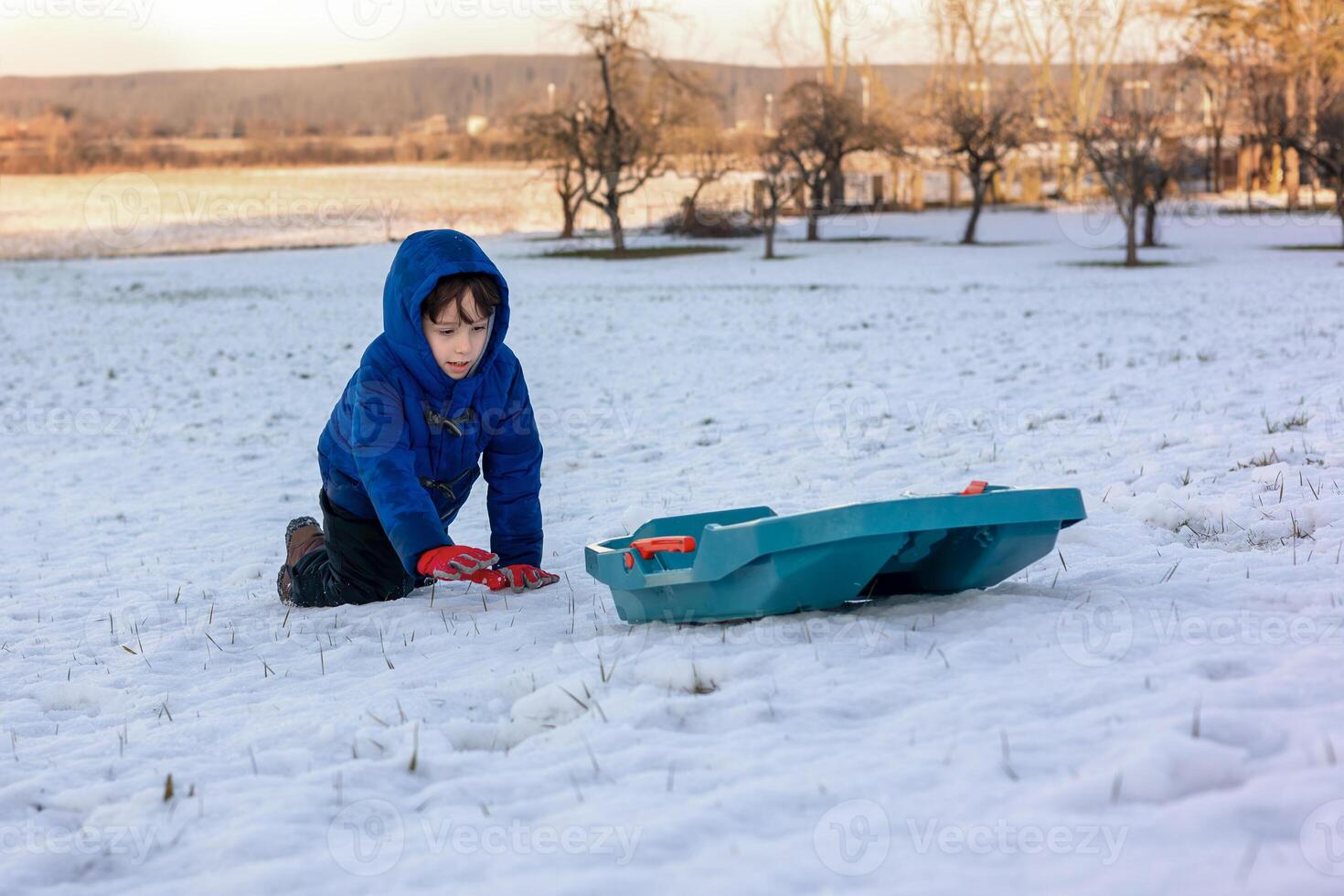 Child playing with sled in snowy landscape during winter day. World Snow Day photo