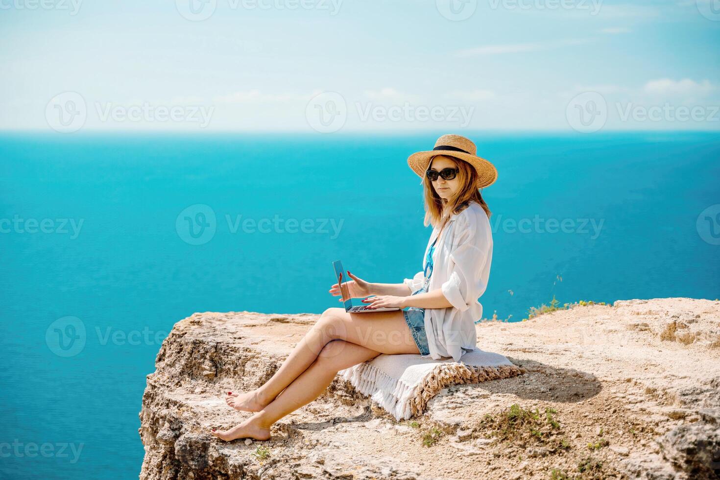 Freelance woman working on a laptop by the sea, typing away on the keyboard while enjoying the beautiful view, highlighting the idea of remote work. photo