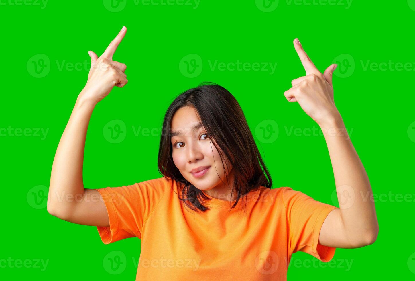 Young woman in orange shirt making playful gestures against a green backdrop in a lively indoor setting photo