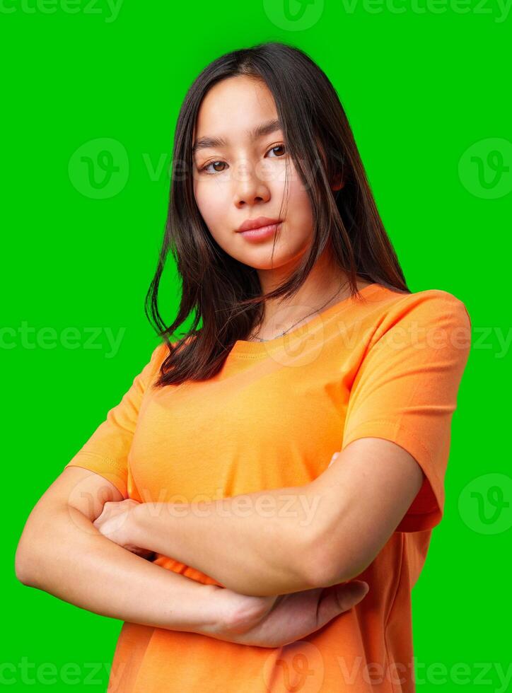 Confident young woman in orange shirt poses with arms crossed against a bright green background photo