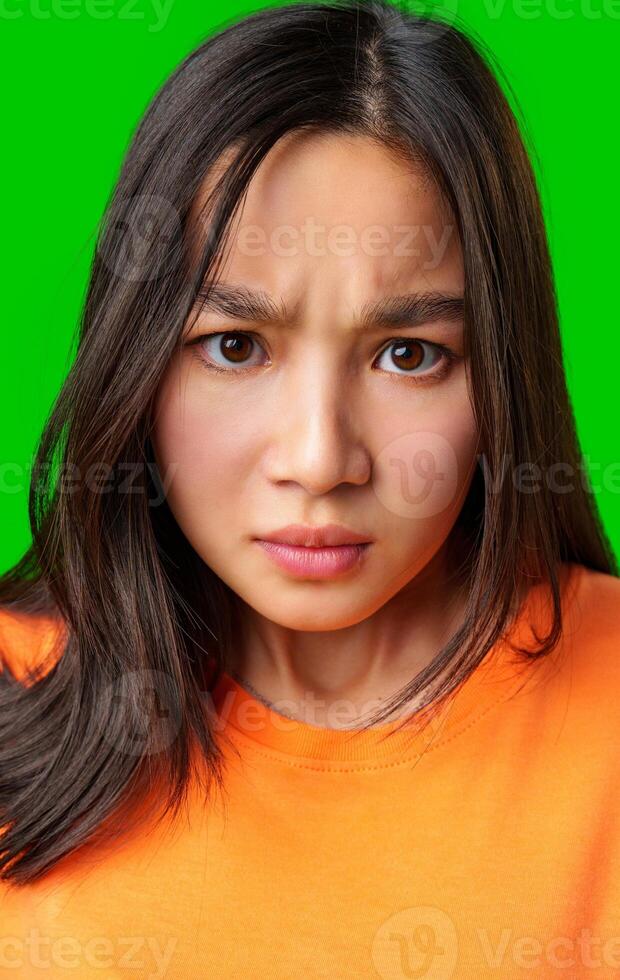 Woman with serious expression wearing orange shirt against bright green background photo