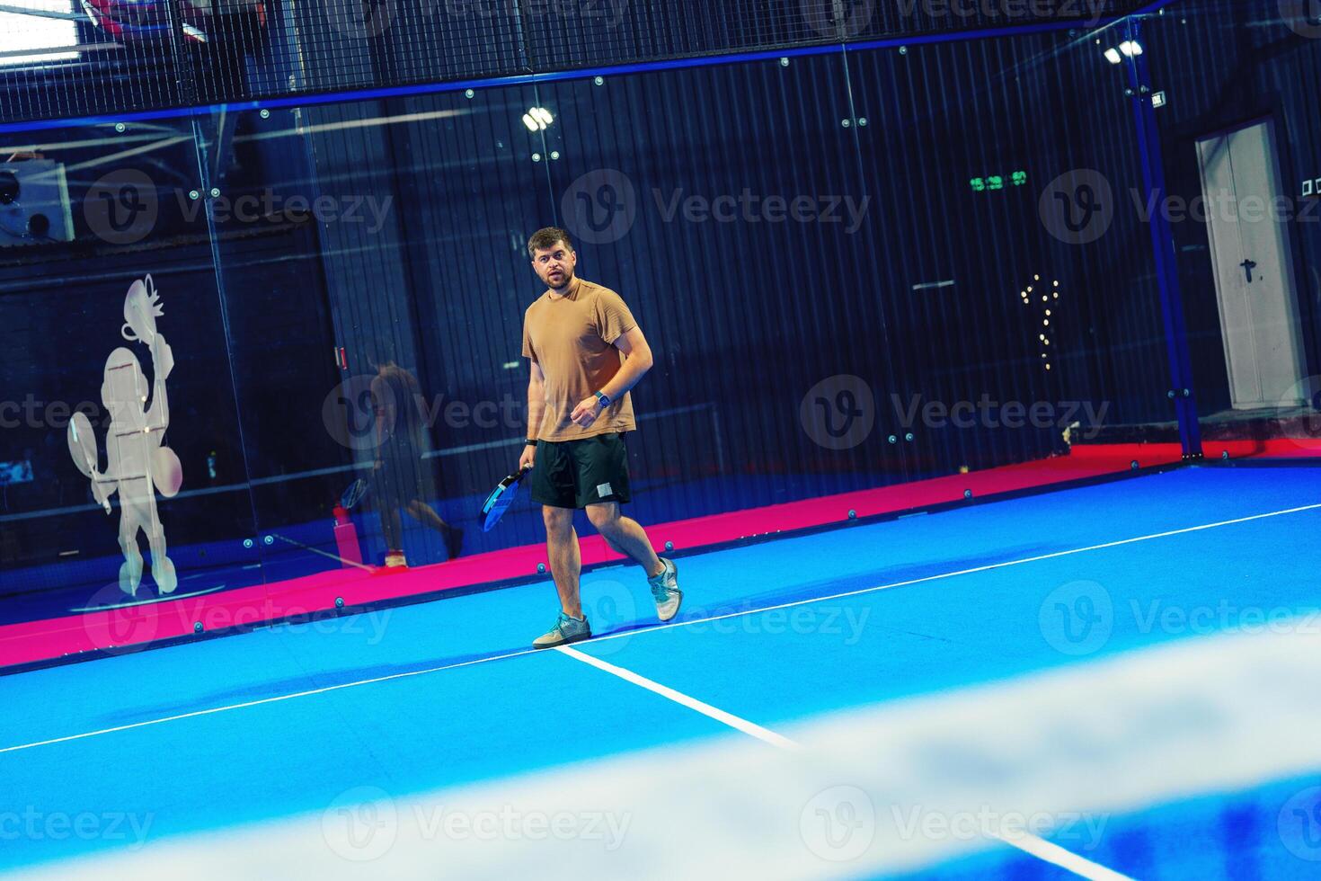 Young man plays padel tennis on a vibrant blue court during a recreational match in an indoor facility photo