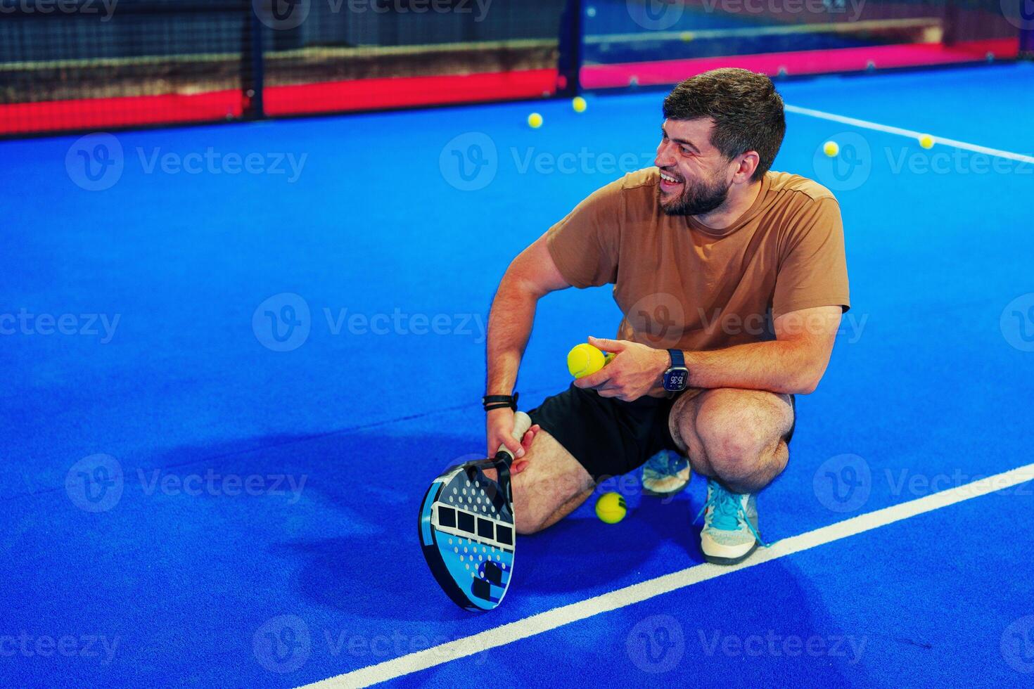 Man practices skills on vibrant blue court while holding paddle and balls during recreational session photo
