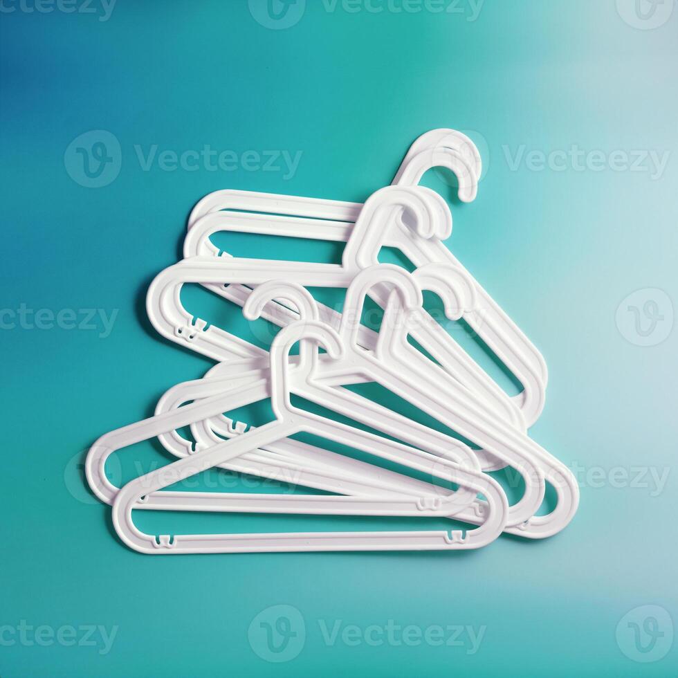 Group of White Plastic hangers as minimal layout on soft gradient background of teal tones, Clothes rack for organizing clothes in closets or retail stores for hanging of garments, top view photo