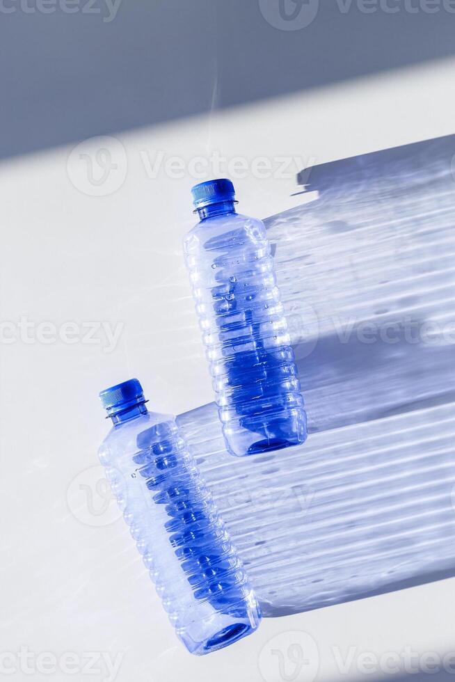 Blue plastic bottles at sunlight shadow on blue white background, top view empty plastic bottle for water half litre, minimal design. Pollution, plastic garbage, environmental protection concept photo