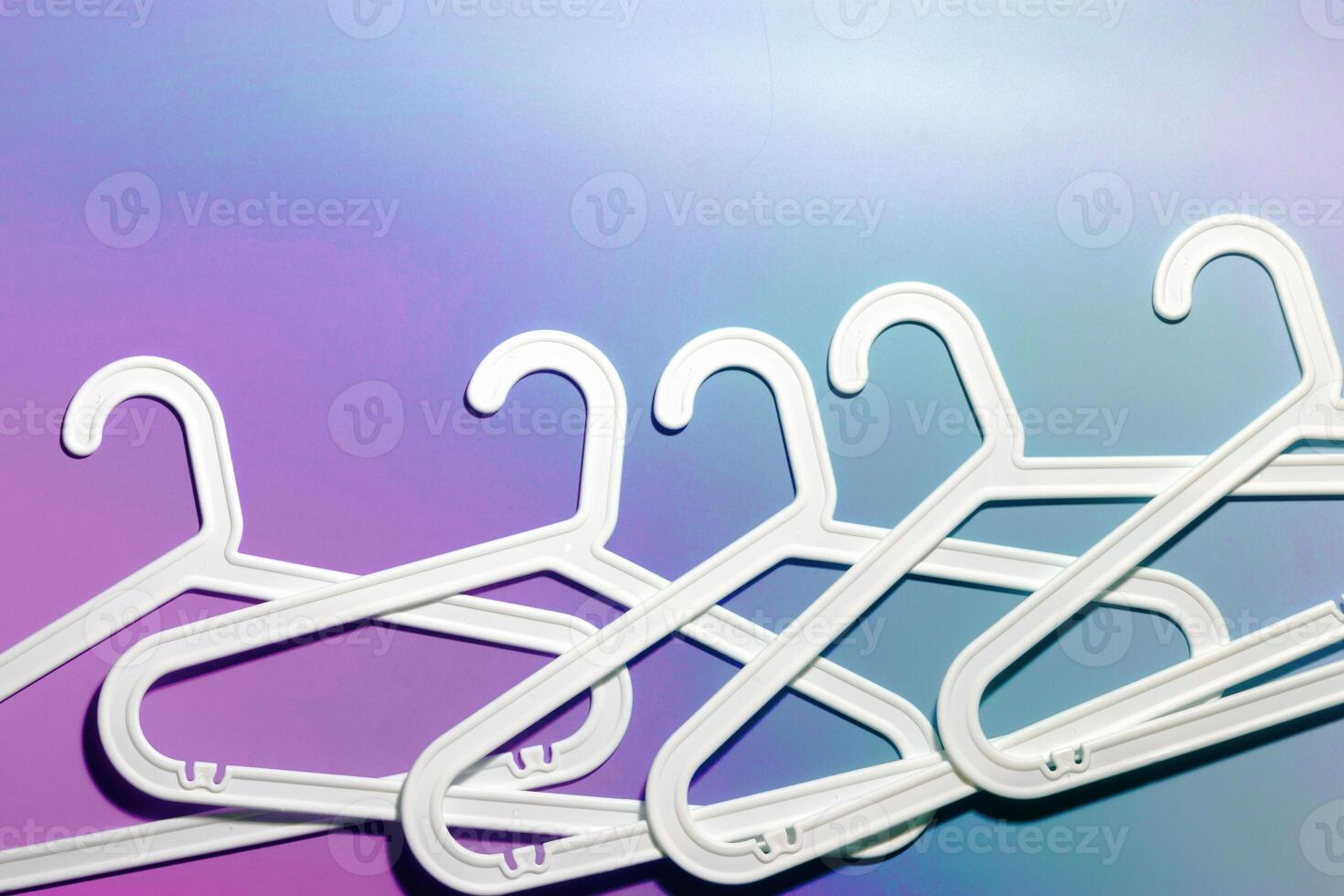 Top view minimal style pattern of white plastic hangers with hook on purple blue background. Flatlay with Clothes racks for hanging garments. Minimal trend photo, lifestyle or interior design content photo