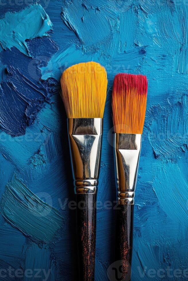 Two paintbrushes resting on vibrant blue painted canvas photo