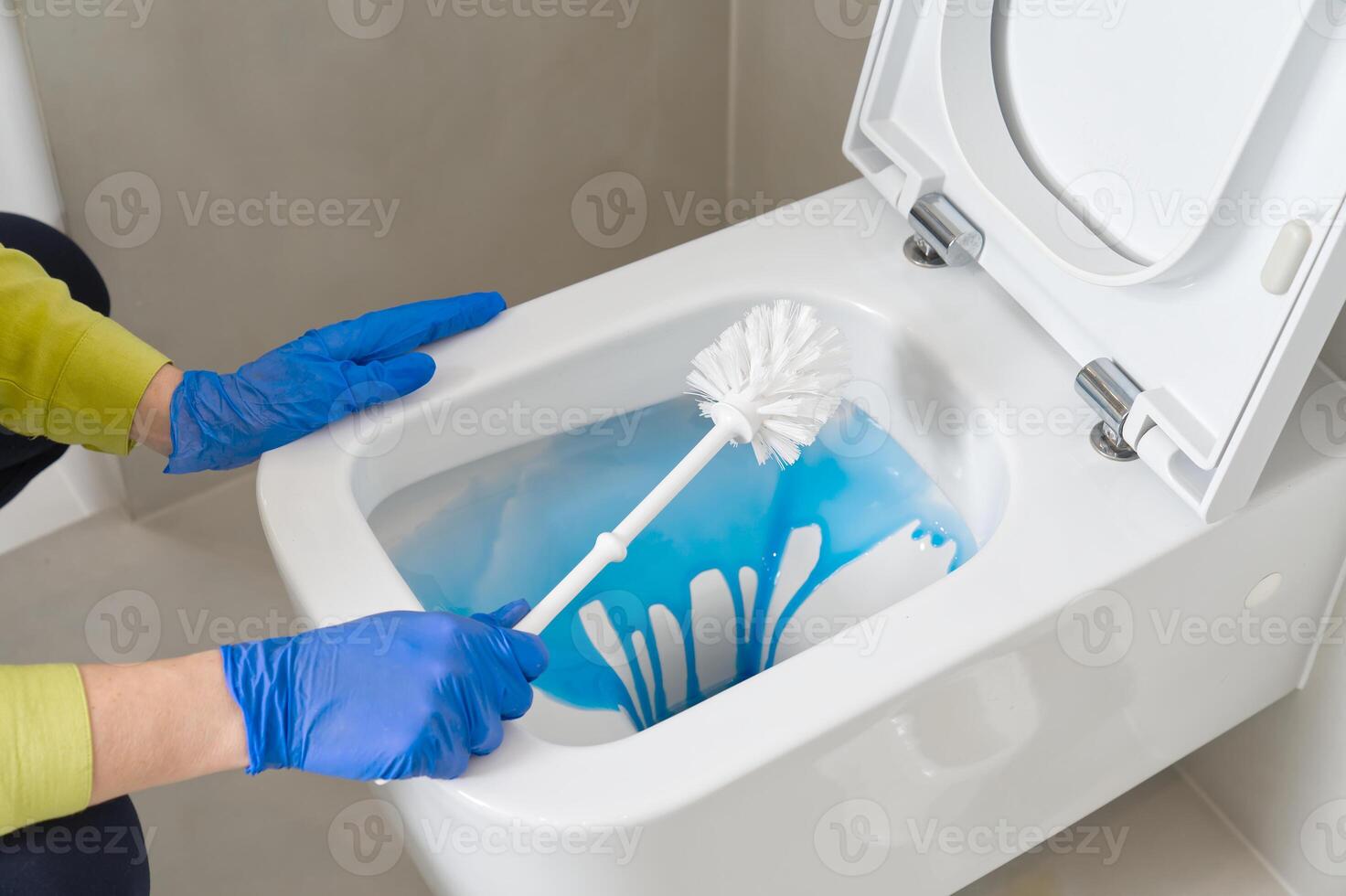 Wall mounted toilet cleaning with detergent. Woman hotel maid cleans a bathroom toilet with a scrub brush. household service. Modern flush toilet. Cleaning photo
