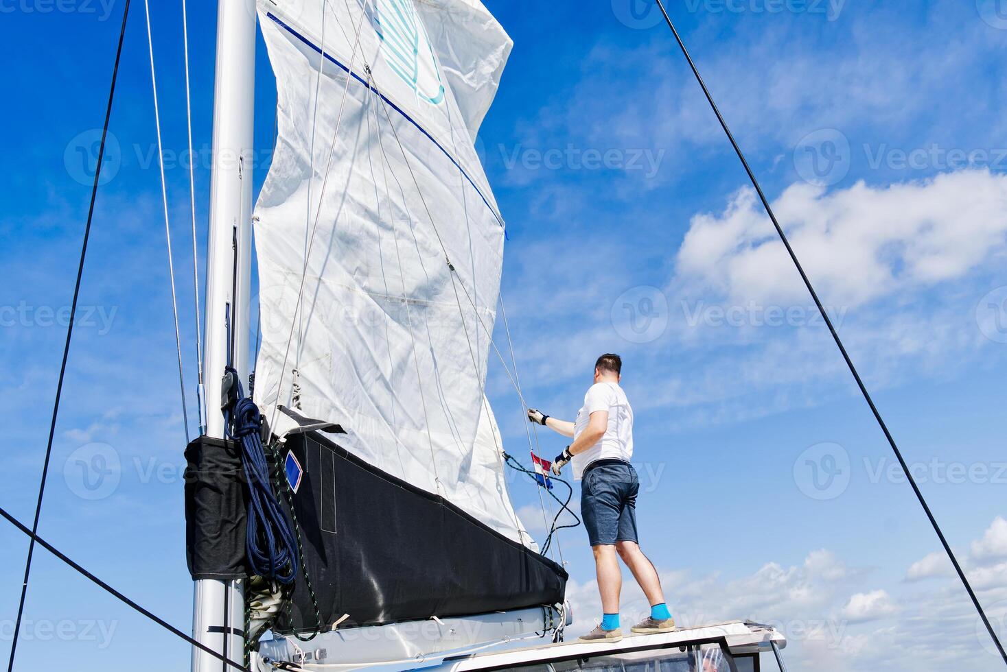 Raising the sail on a yacht. Young man captan lifting the sail of catamaran yacht during cruising. luxury sailing yacht, with sails being raised by rigging photo