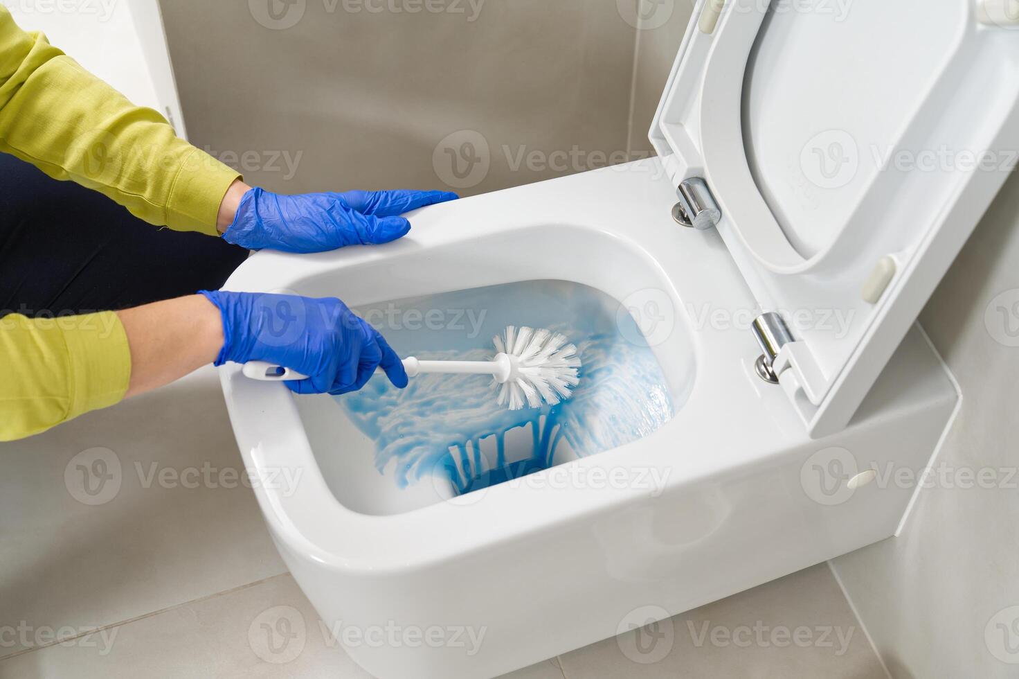 Wall mounted toilet cleaning with detergent. Woman hotel maid cleans a bathroom toilet with a scrub brush. household service. Modern flush toilet. Cleaning photo