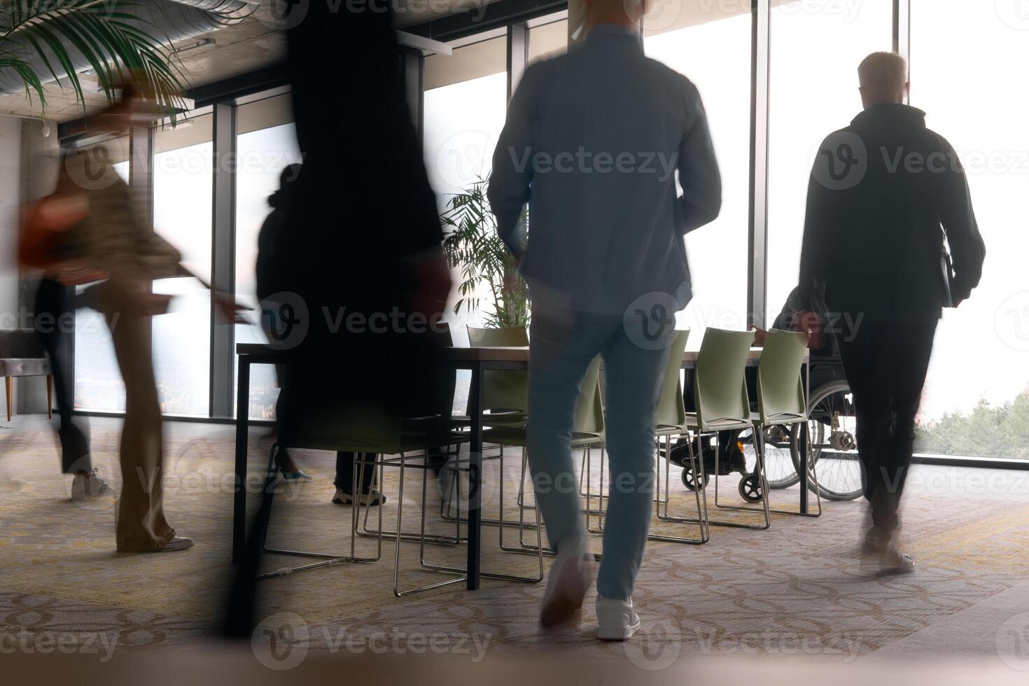 A diverse business team, working urgently around a conference table, collaborates on a meeting while their director, seated in a wheelchair, waits for their input photo