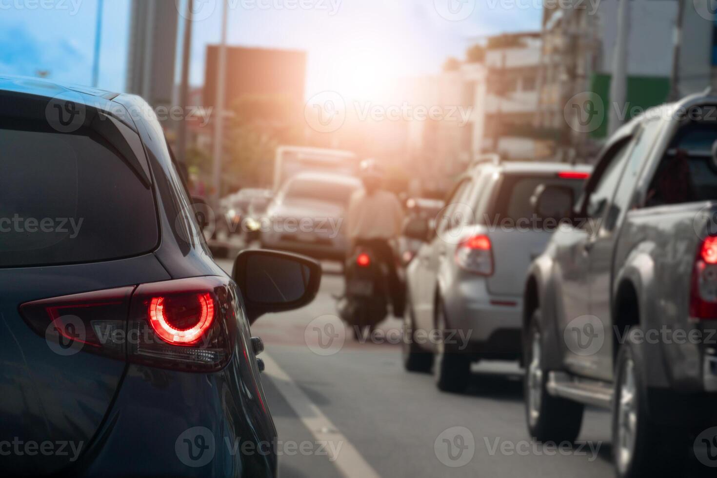 Rear side view of black car driving on the road. Background blurred of other cars under sky in the city. Cars lined up on the road in urgent traffic condition. Stop by traffic light. photo