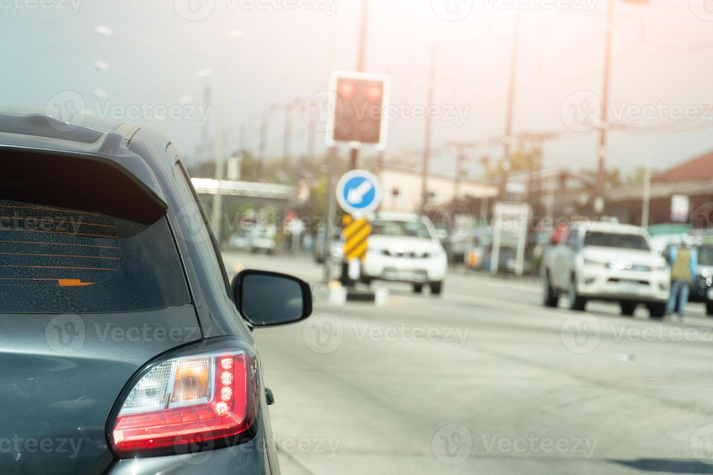 Rear side view of gray car. Body of car with dust of rain on the glass. wtih turn on brake light and turn signal light. Conretet road with traffic signal. Opposit of road with cars line up in a queue. photo