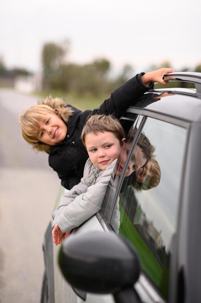 Playful boys hang out of the car window, smiling and catching the wind on a road trip. photo