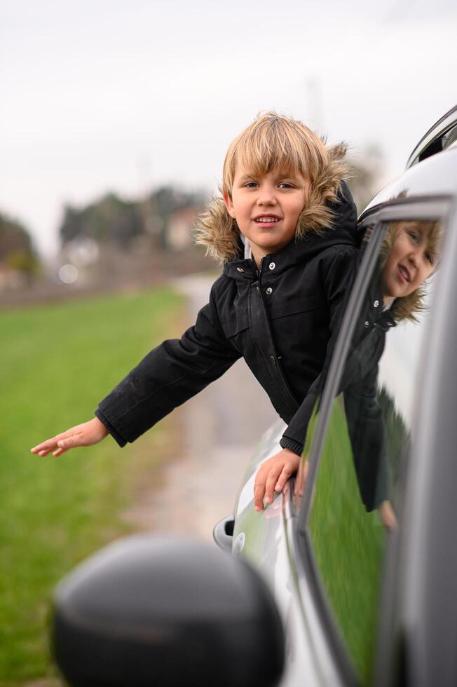 The small boy, excited and carefree, leans out of the window, enjoying the scenery on a road trip. photo