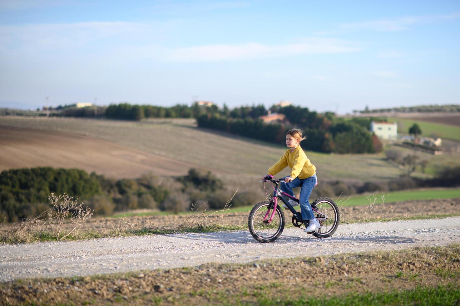 A girl rides her bicycle on a rural road, surrounded by fields, enjoying the countryside. photo