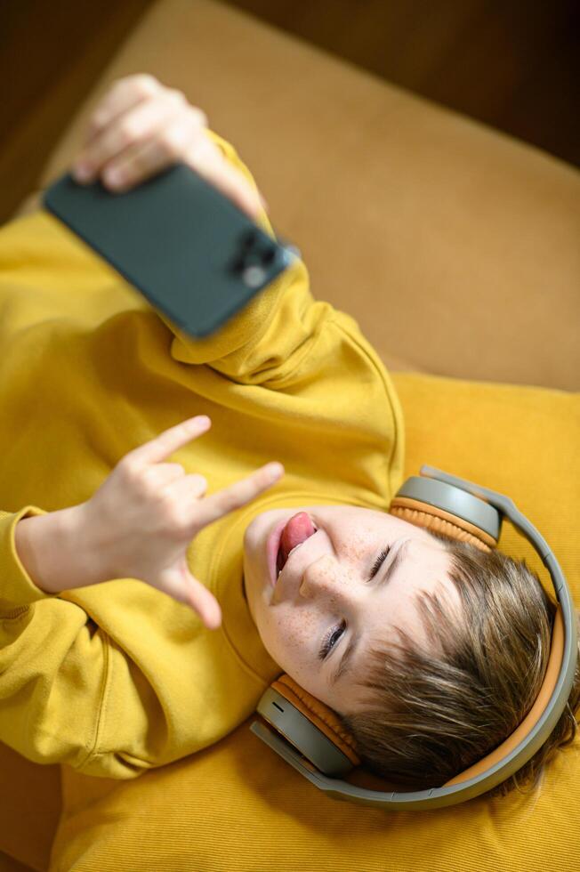 Relaxing on a yellow couch, a boy in yellow listens to music with his phone in hand photo