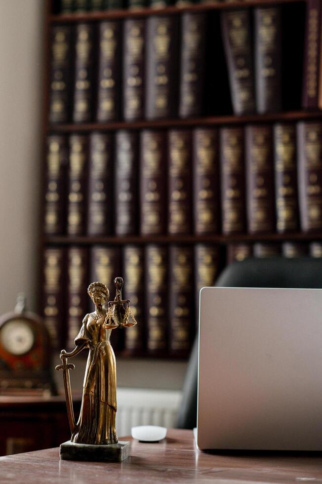 A refined legal workspace with a grand bookshelf packed with law books, a well organized desk, and a bronze statue of Themis holding her scales and sword photo