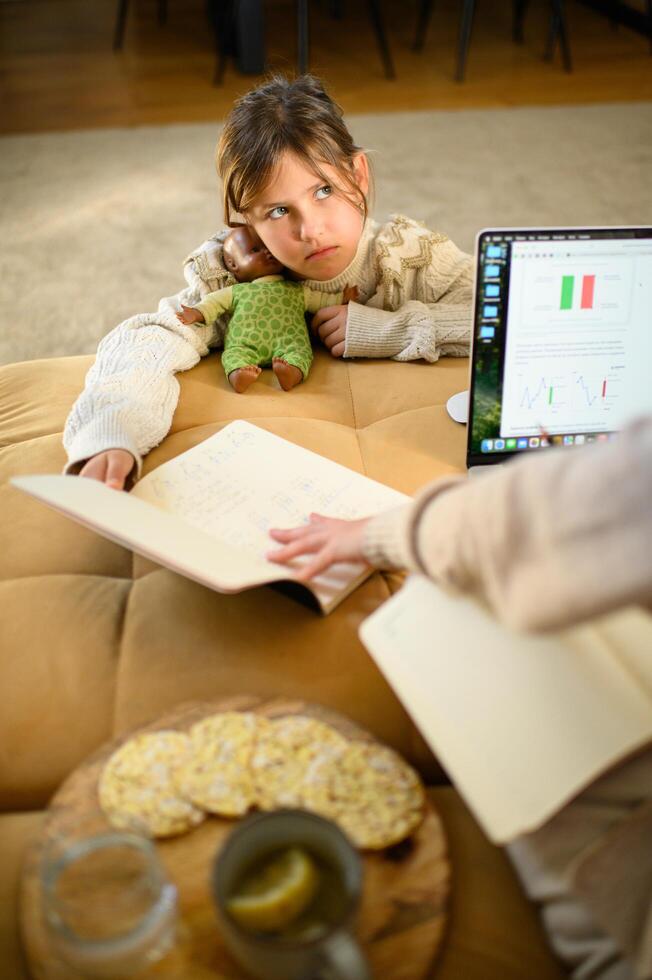 While her mother works on the computer, the girl is excitedly waiting to spend time with her. photo