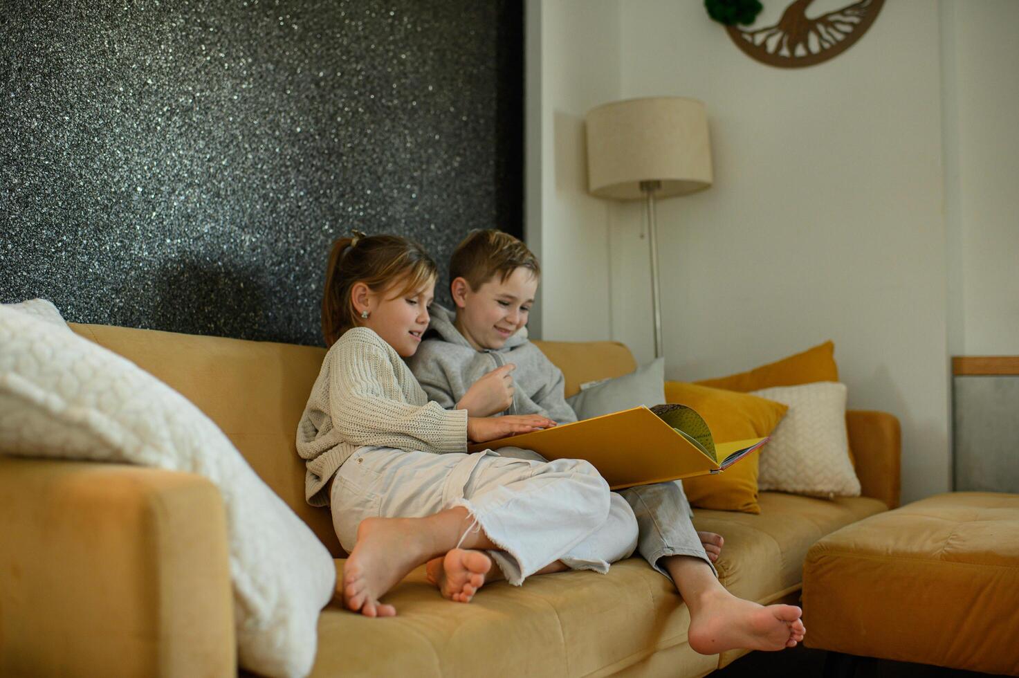 A boy and girl sit together on the couch, reading a book, absorbed in the story. photo