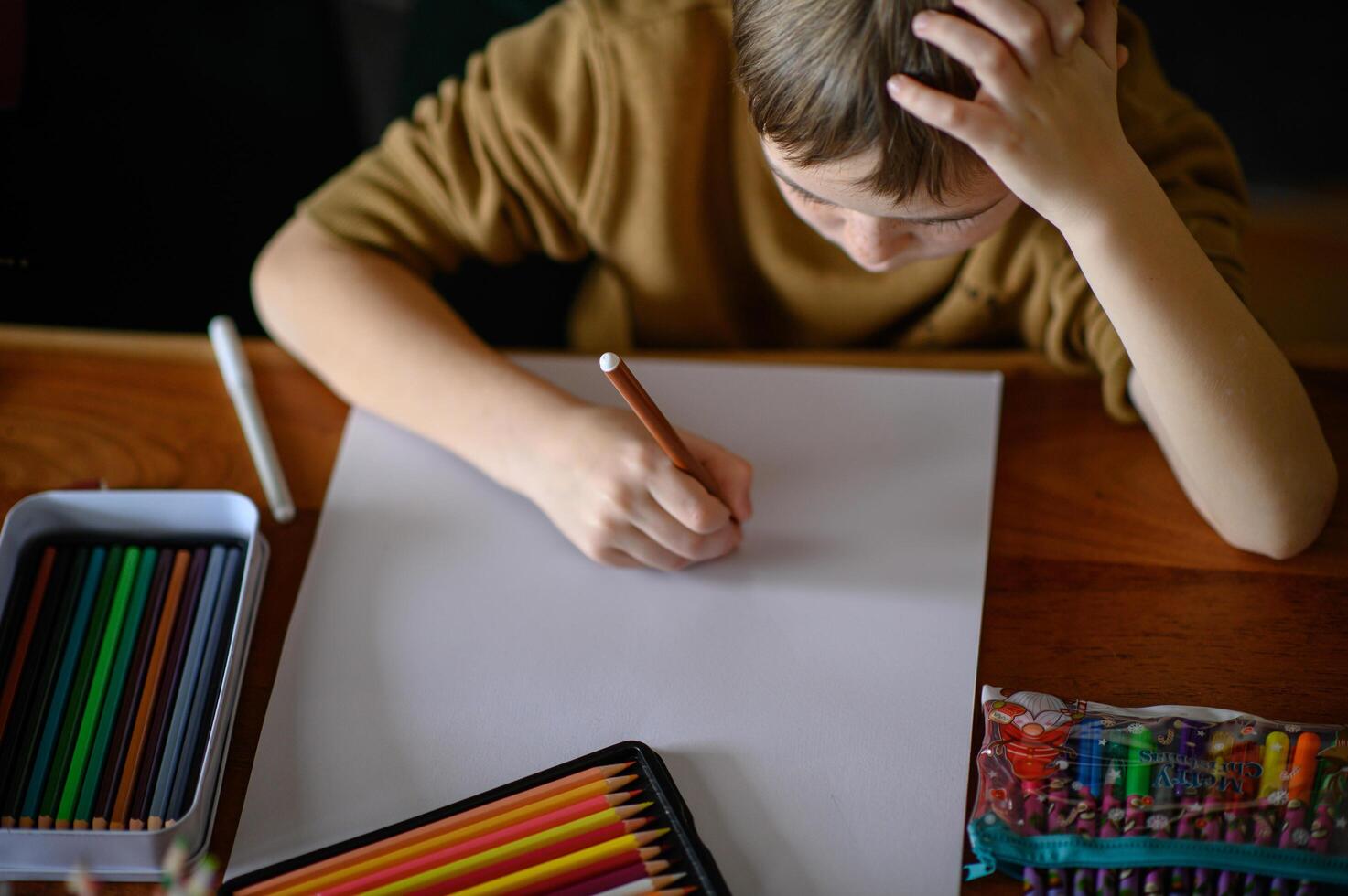 With crayons and markers scattered on the table, the boy thinks about his next idea. photo