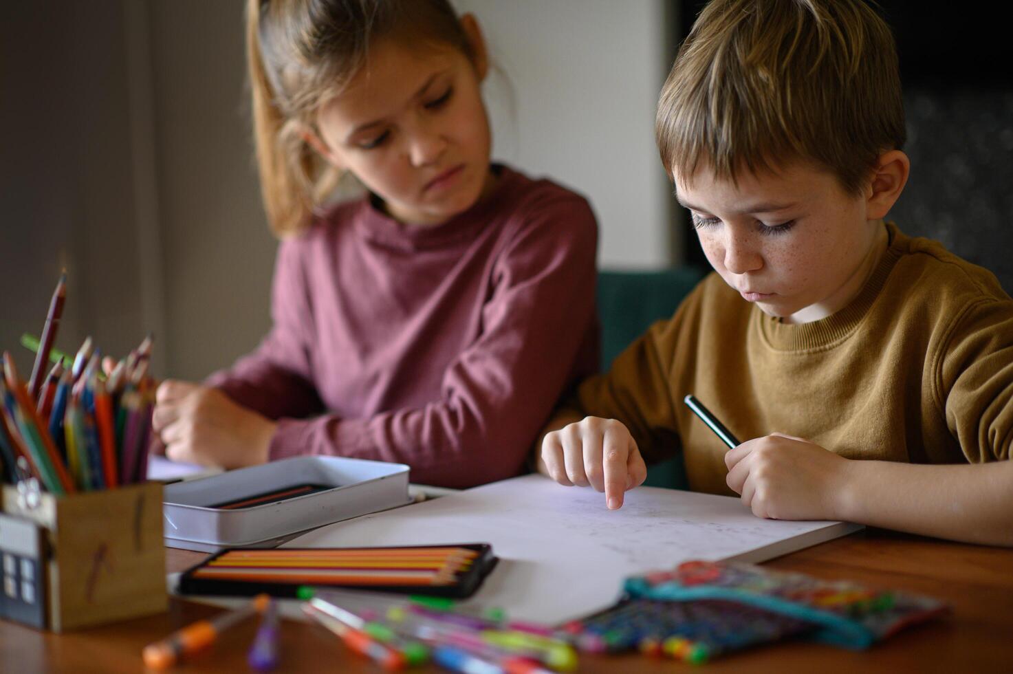 A brother and sister sit side by side, surrounded by art supplies, deciding what to draw next. photo
