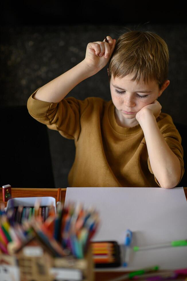 The boy leans over the table, surrounded by colors, lost in creative thought. photo