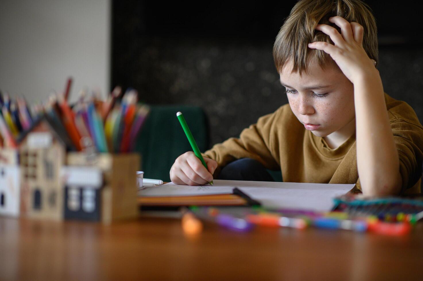 The child sits quietly at the table, contemplating his blank canvas and colorful options. photo