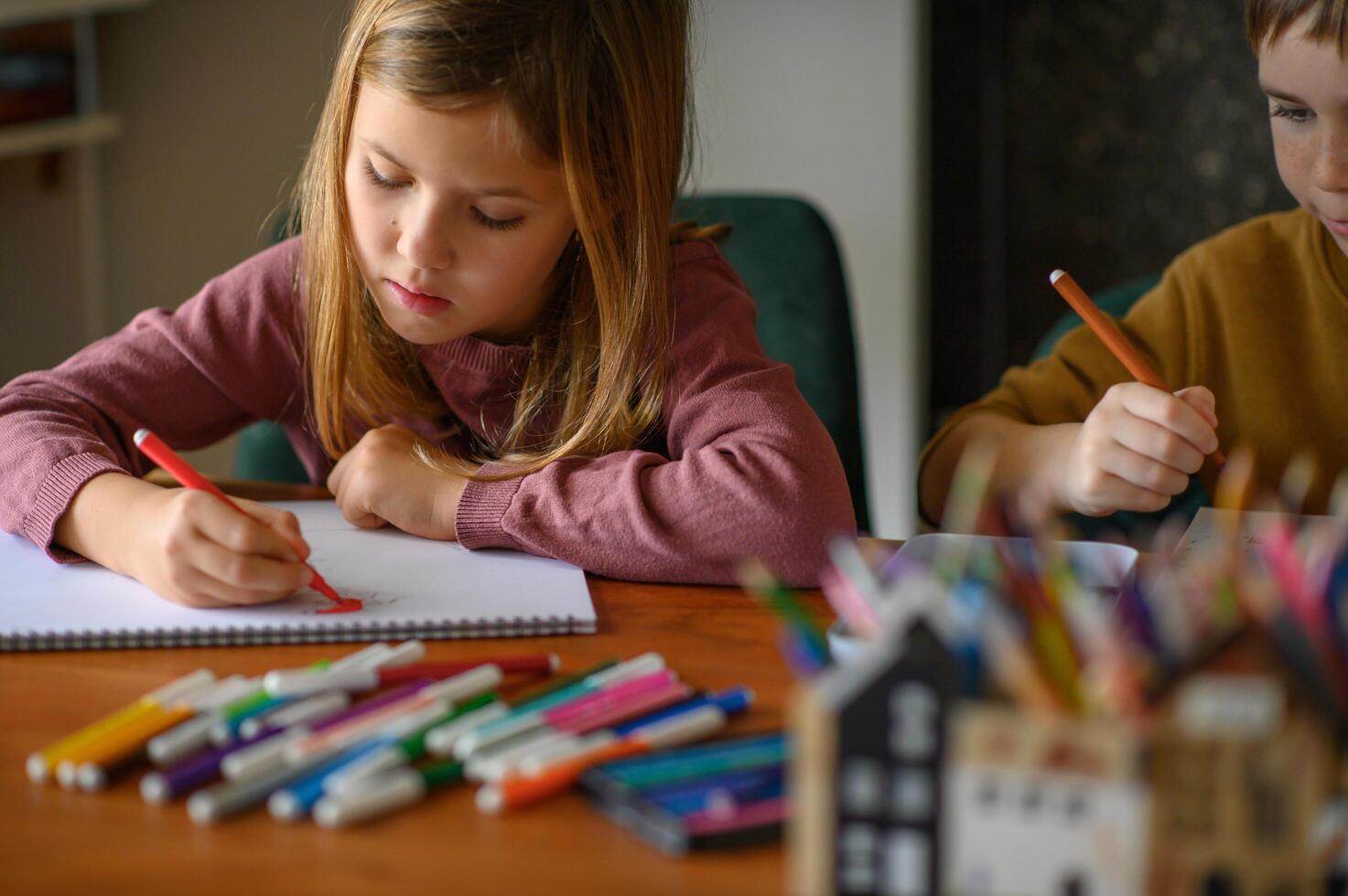 Two children sit quietly at the table, surrounded by art tools, deciding on their creations. photo