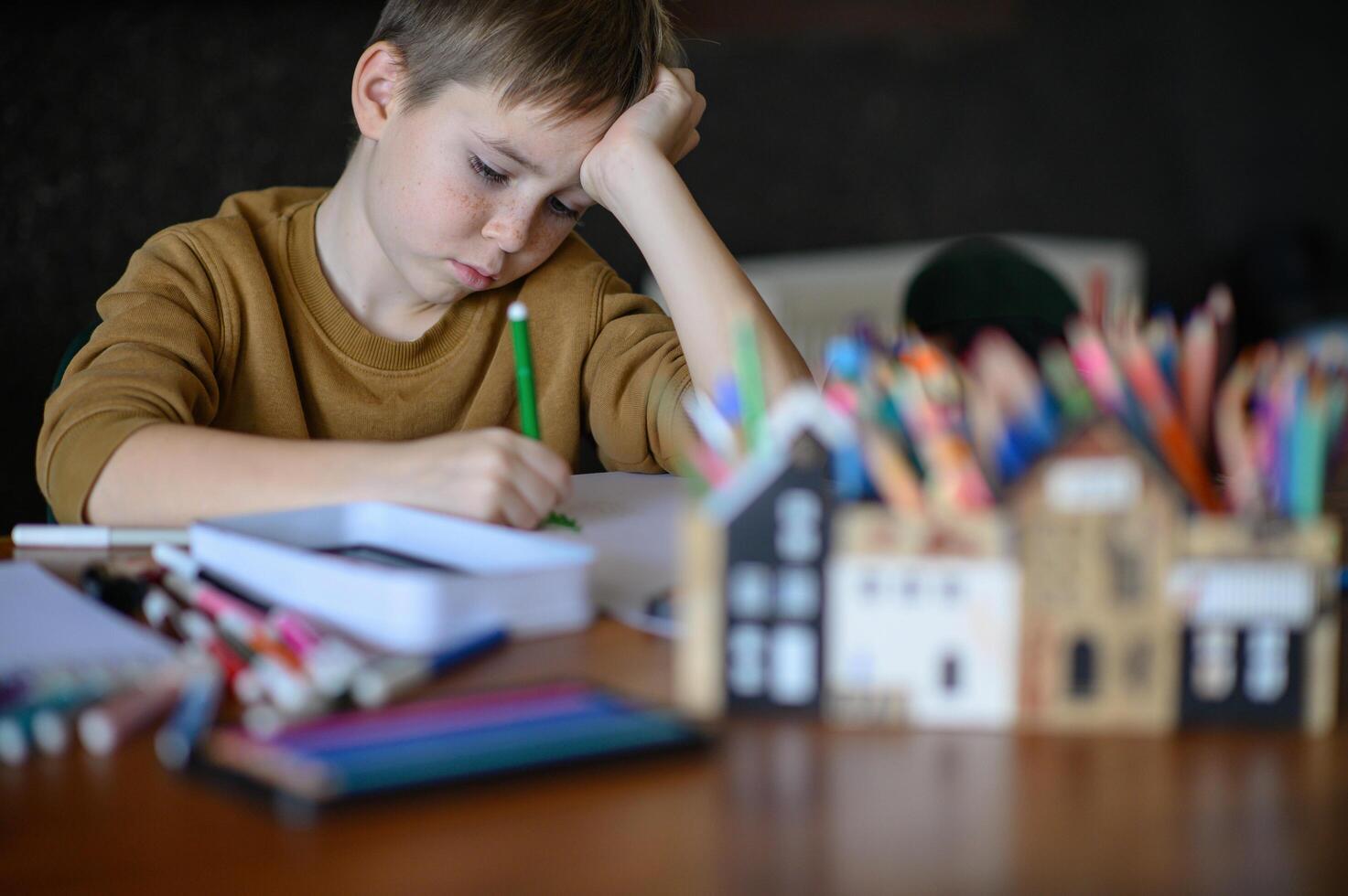 A boy sits at the table with crayons and markers, imagining his next creation on the blank sheet. photo