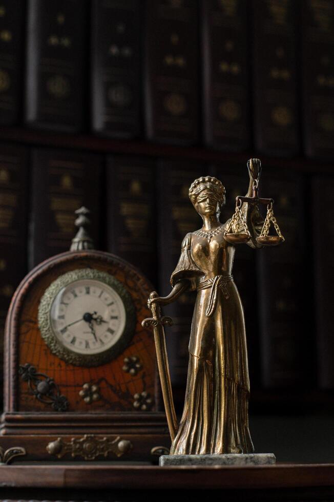 An old-fashioned desk with an ornate antique clock and a detailed statue of Themis holding her scales and sword. photo