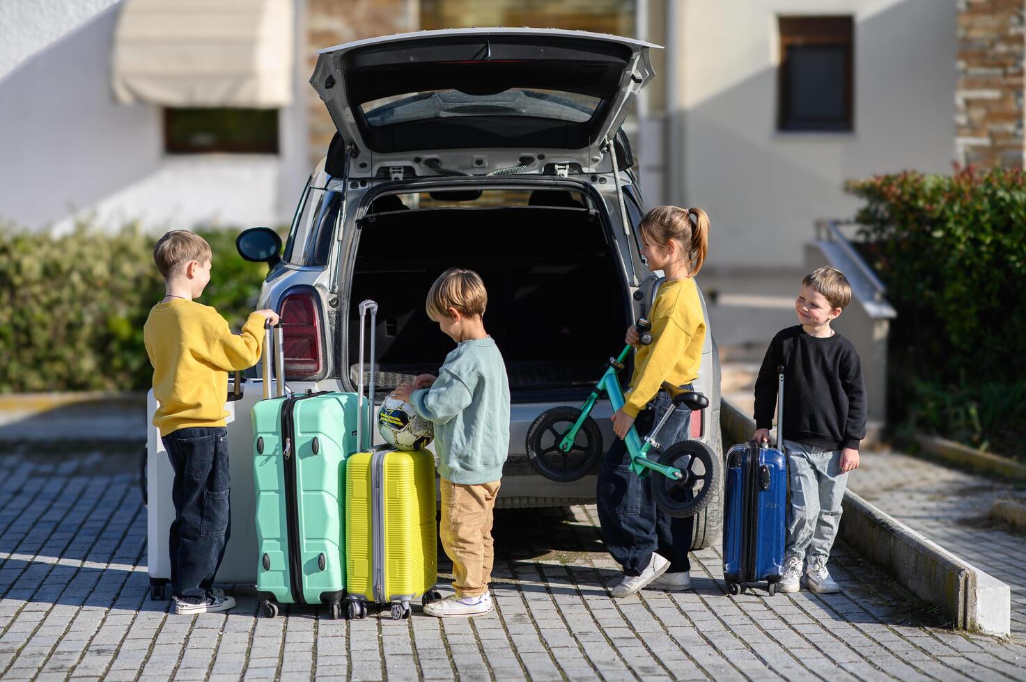 Four children excitedly gather by the open trunk, where vibrant suitcases and scooters are ready for the trip. photo