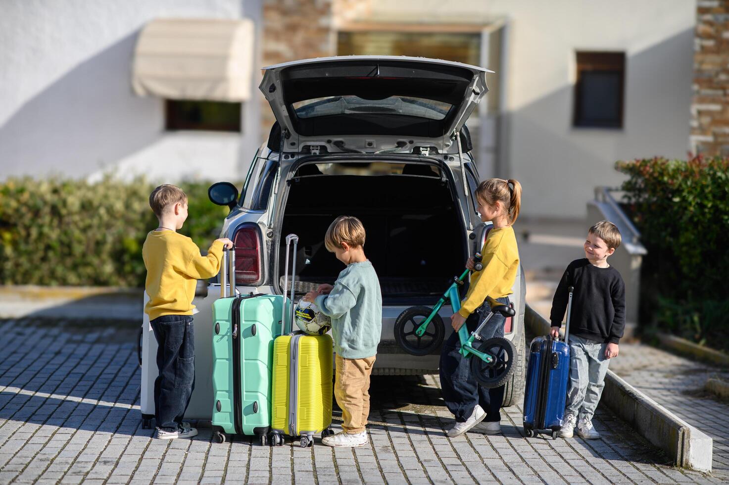By the cars open trunk four kids laugh and talk as they get ready for a journey with their scooters and suitcases photo