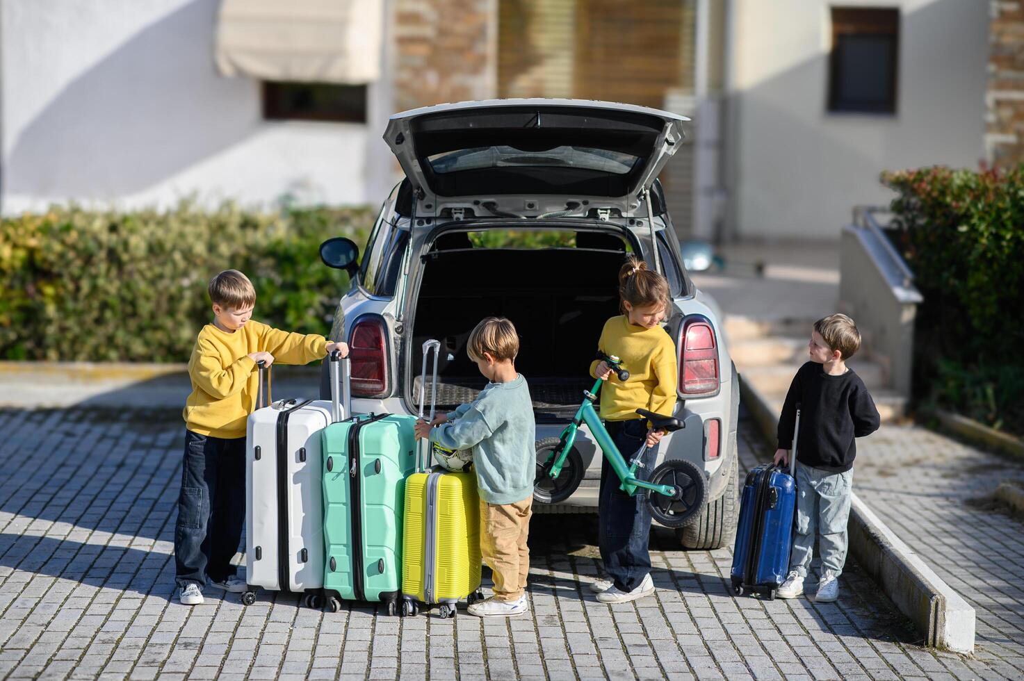 Four children stand near a packed car trunk, ready for an adventure with their bright luggage and scooters photo