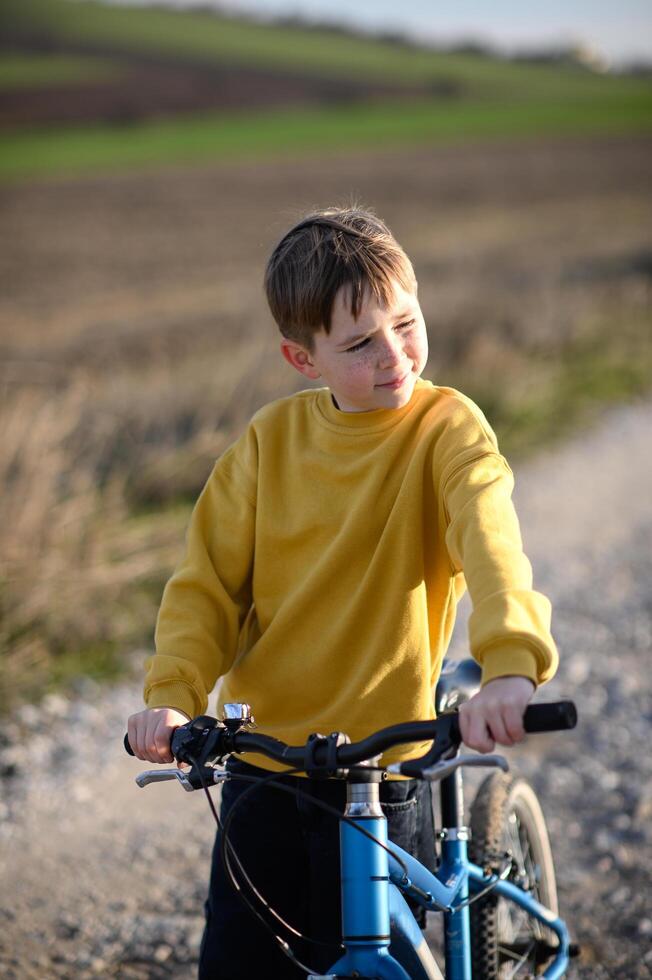 A boy with his bicycle on a rural road, surrounded by fields, on a sunny, warm day. photo