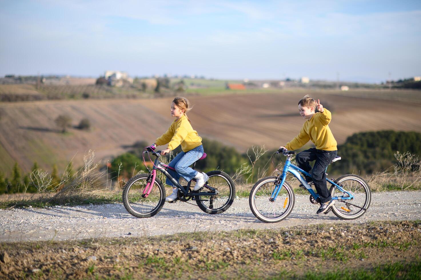 Two kids cycle along a rural path, surrounded by fields, on a bright and sunny day. photo