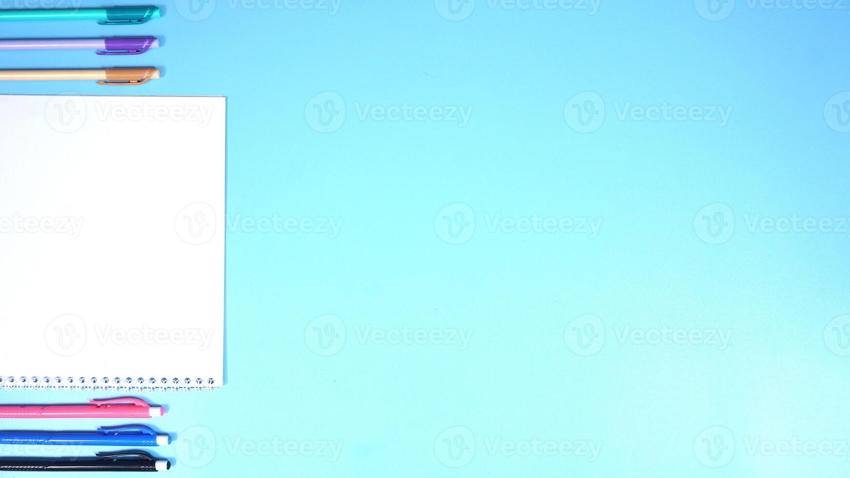 Various Color of Pens and Notebook on Blue Background photo