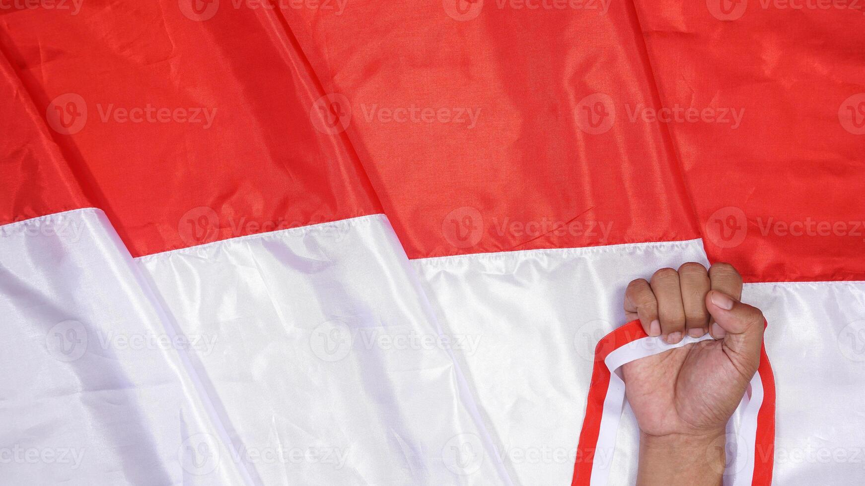 Red and White National Flag of Indonesia as Background for Copy Space with Man's Hand Holding Red and White Ribbons photo