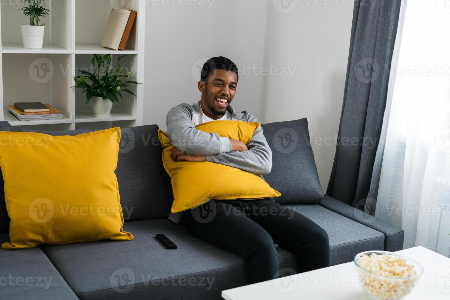Cheerful curly haired ethnic african american male in casual clothes resting at home on comfortable sofa while watching tv channels or movie during weekend. Tv set, online television and entertiment photo