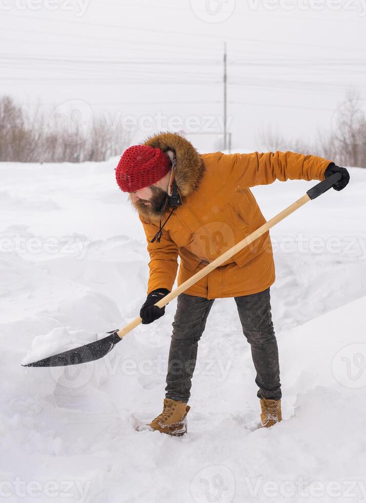 Young man clearing snow in his backyard village house with shovel. Remove snow from the sidewalk. photo