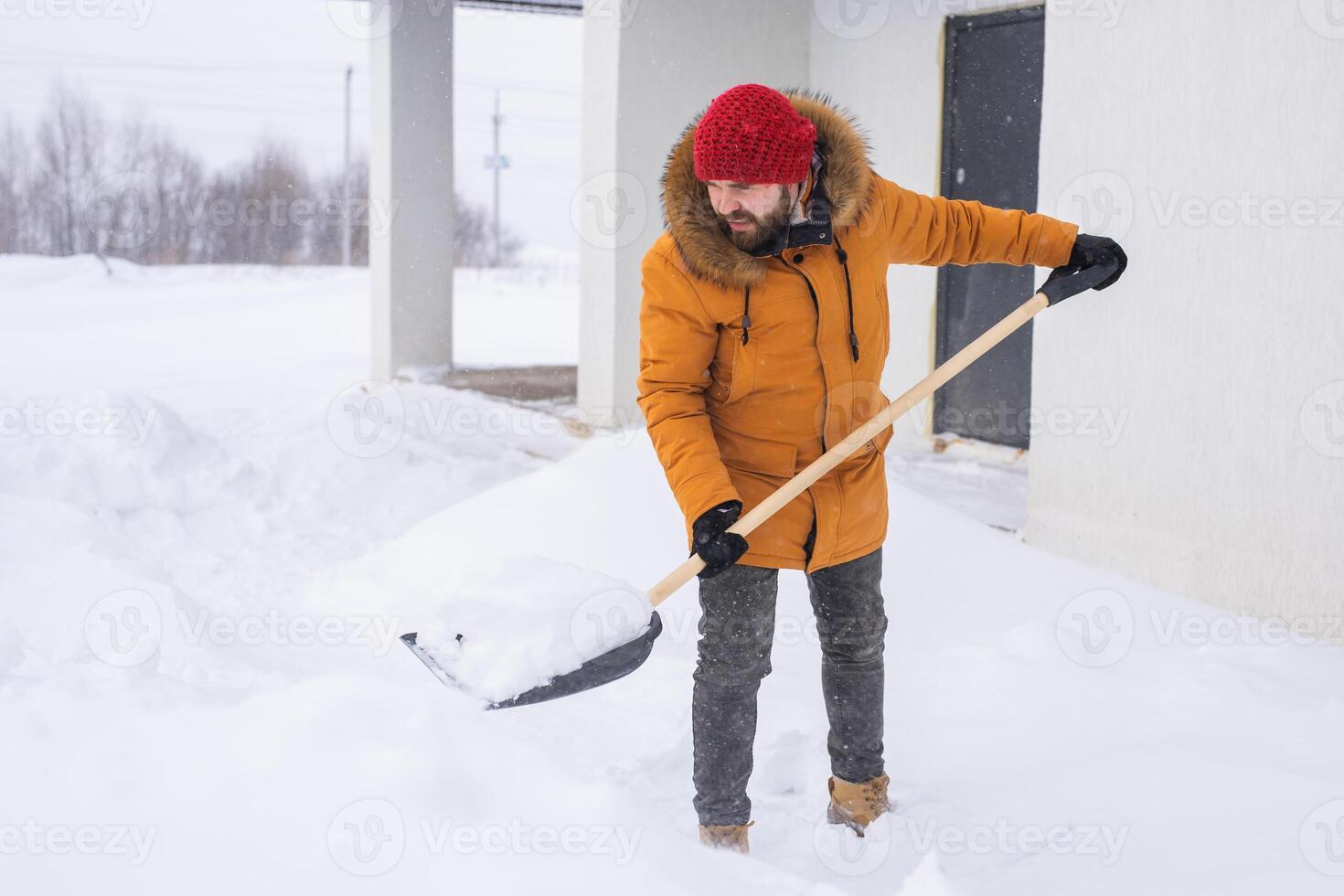 Young man clearing snow in his backyard village house with shovel. Remove snow from the sidewalk. photo