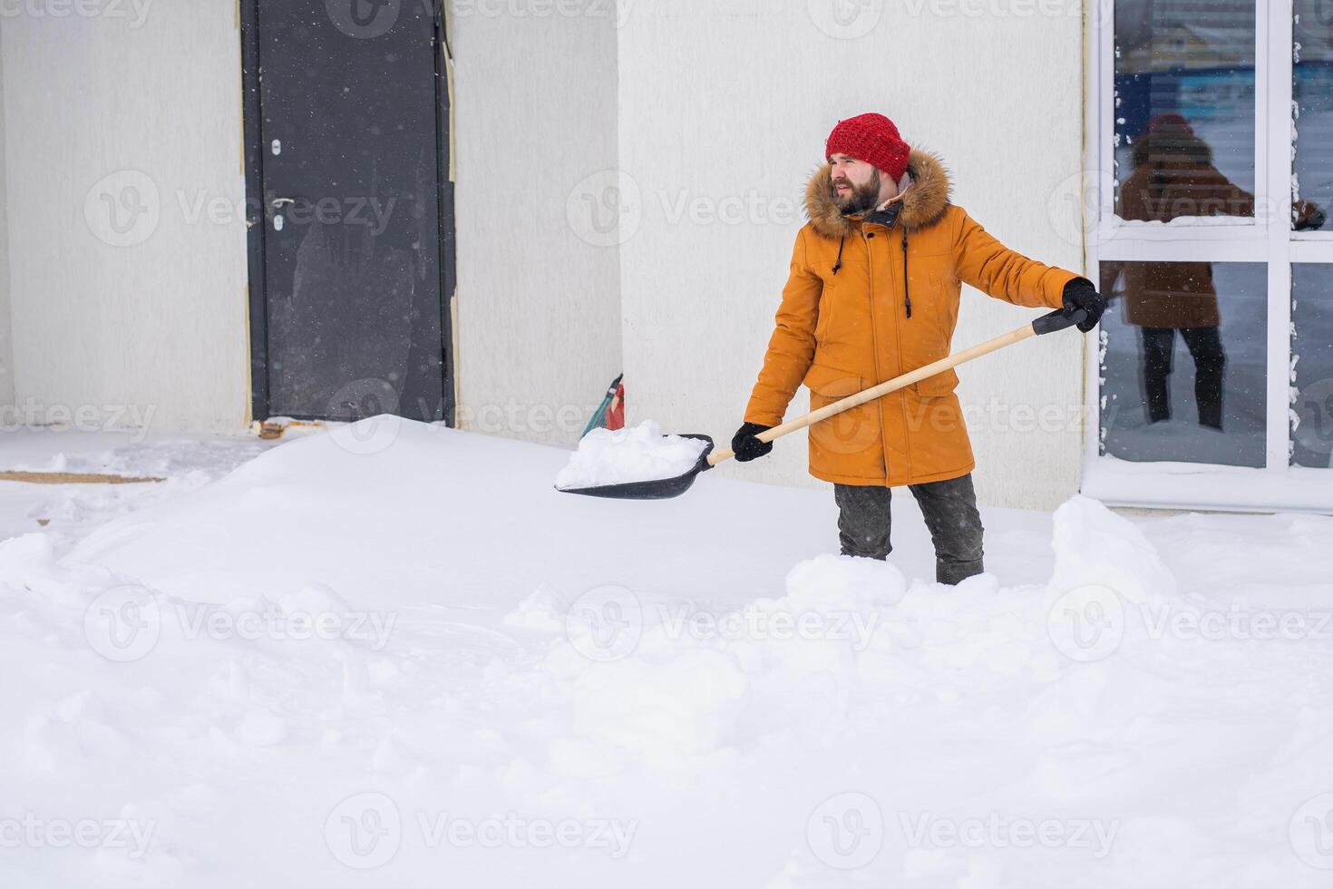 A man cleans and clears the snow in front of the house on frosty day. Cleaning the street from snow on a winter day. Snowfall and severe snowstorm in winter. photo