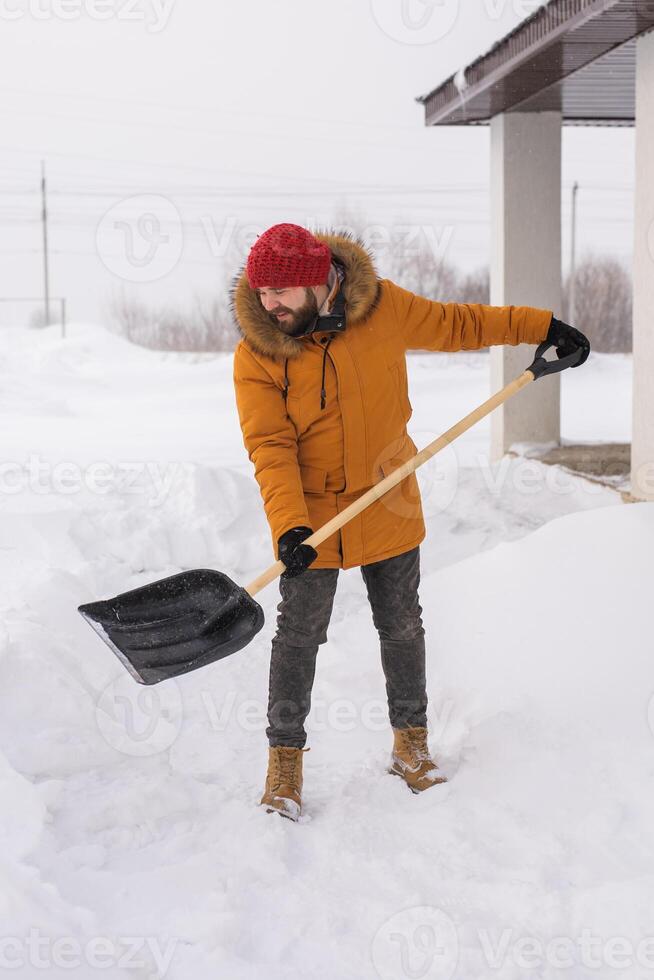 A man cleans and clears the snow in front of the house on frosty day. Cleaning the street from snow on a winter day. Snowfall and severe snowstorm in winter. photo