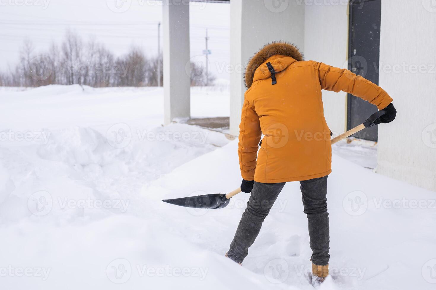 Young man clearing snow in his backyard village house with shovel. Remove snow from the sidewalk. photo